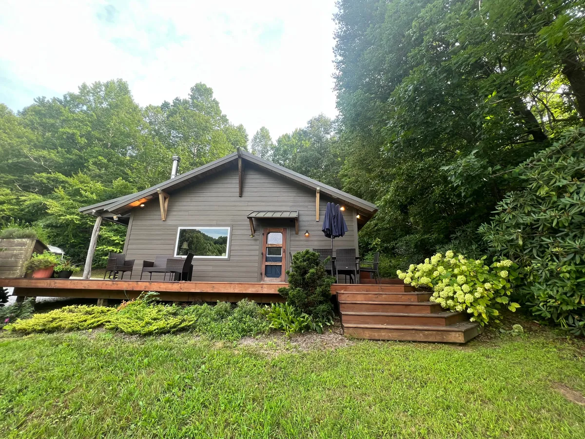 A tranquil wooden deck overlooking green shrubbery, with ample outdoor seating and a large window connecting to the home. The setup highlights opportunities for group relaxation, morning coffees, and connection to the surrounding landscape.