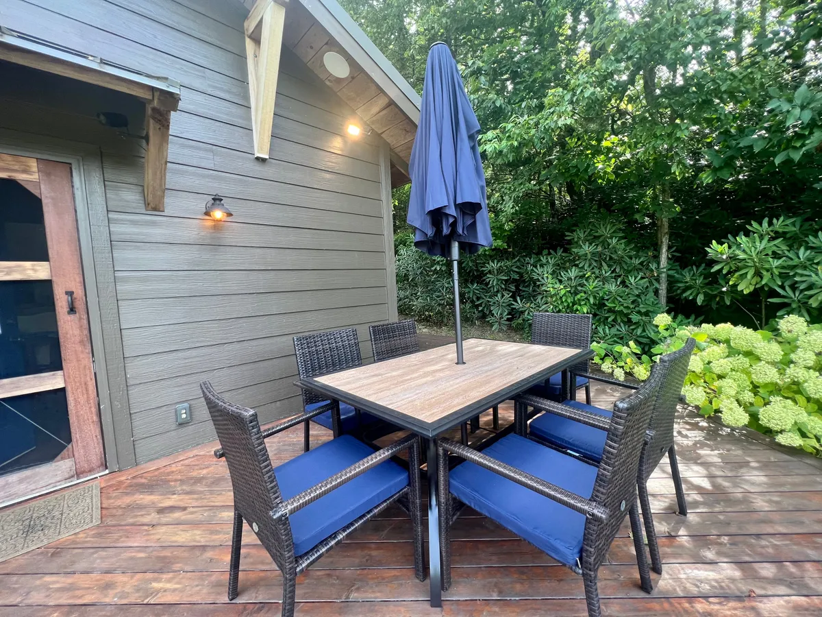 A relaxed outdoor dining area featuring a table with an umbrella, surrounded by greenery. The setup invites families to enjoy meals and downtime in the open air, with a casual, welcoming mood ideal for gatherings or a post-adventure picnic.