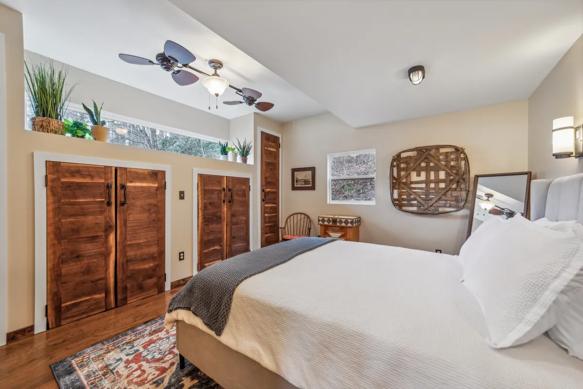 A serene sleeping area with a bed dressed in white bedding, surrounded by wooden storage cabinets, decorative wall art, and bathed in natural light from nearby windows. The scene radiates calm and makes clear the Airstream’s capacity for restful, private nights.