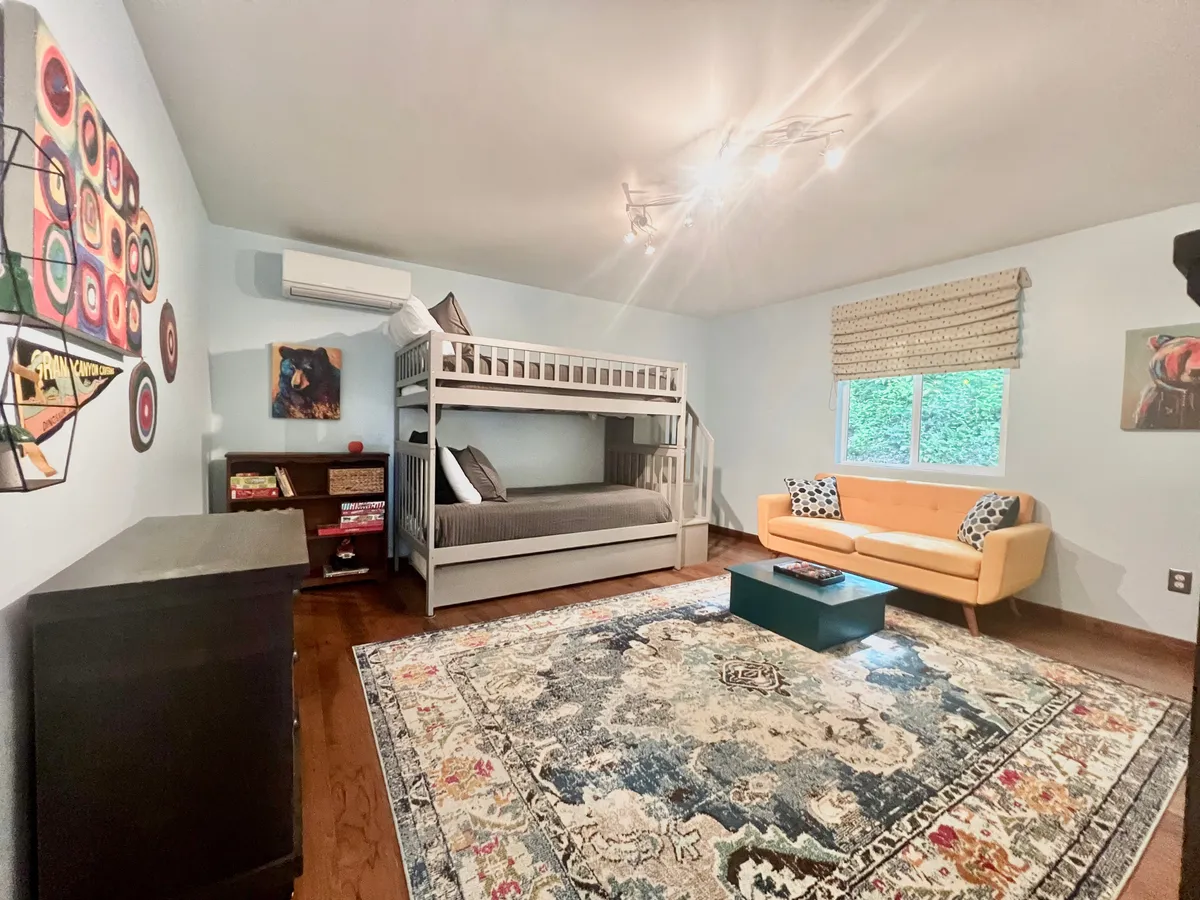 A playful and cozy bedroom featuring a twin bunk bed, an orange sofa, a decorative rug, and artwork on the wall. The space is inviting and designed for both relaxation and play, perfect for children or friends sharing stories and games.