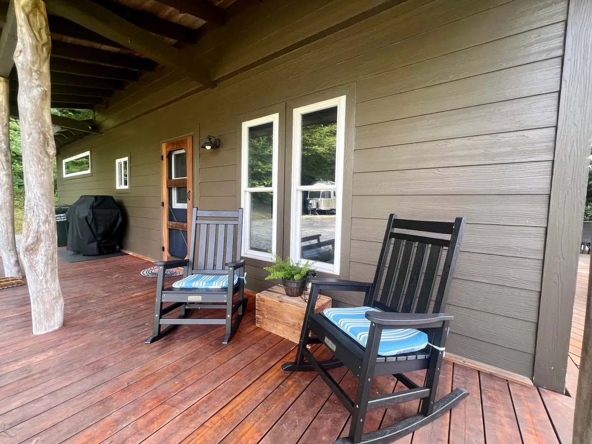 This image features a wooden deck adorned with classic rocking chairs, a planter filled with greenery, and windows reflecting the outdoor light. The scene is tranquil, suggesting a space for both relaxation and socialization, with a direct connection to the fresh mountain air described in the section.